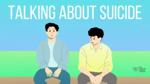 Thumbnail for the blog titled how to talk about suicide. The thumbnail shows a person with blank expression as if in frozen state and there is another person beside him who is trying to talk to him. there is a text behind them for visuals saying - talking about suicide.